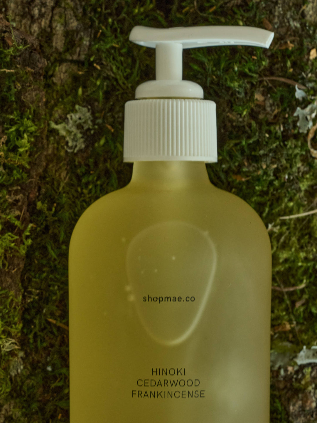 Yellow bottle with white pump labeled 'shopmae.co' on a green mossy background