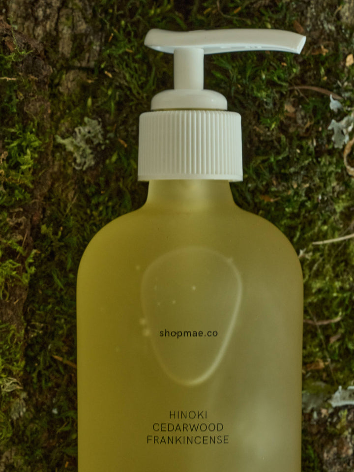 Yellow bottle with white pump labeled 'shopmae.co' on a green mossy background