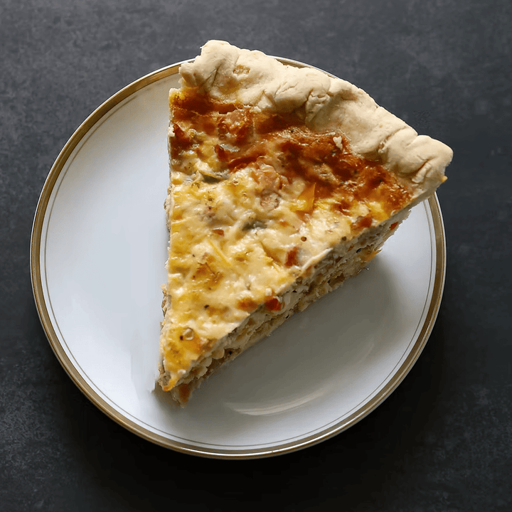Slice of quiche on a white plate with a dark background