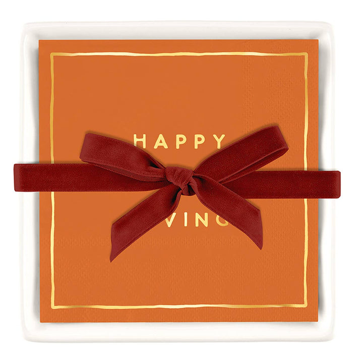 Orange cocktail napkins with gold foil Happy Thanksgiving lettering in a white ceramic tray with a red bow for gifting.  