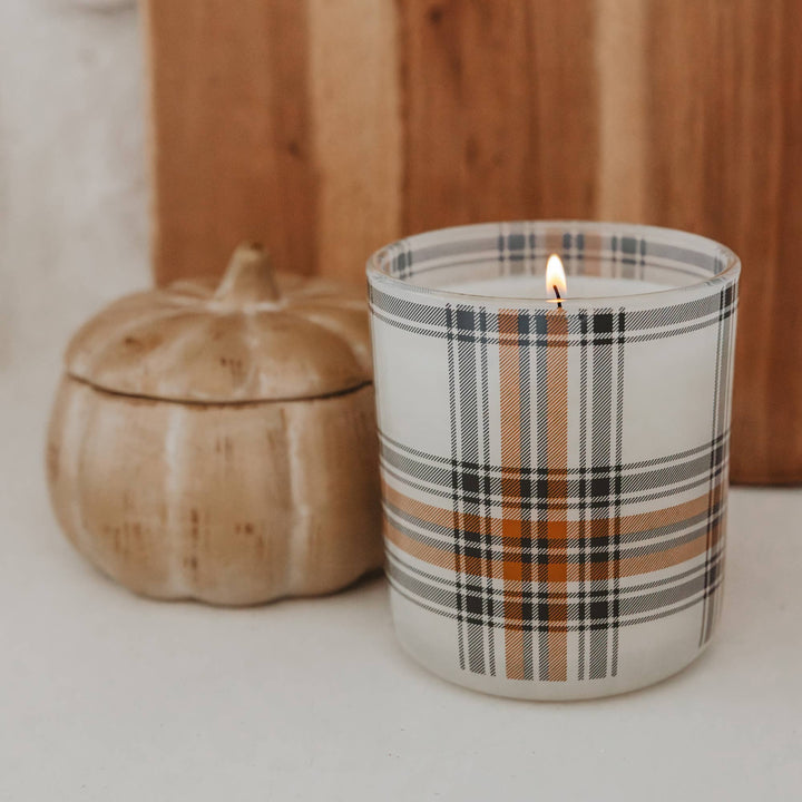 Candle with plaid design next to a pumpkin on a neutral background
