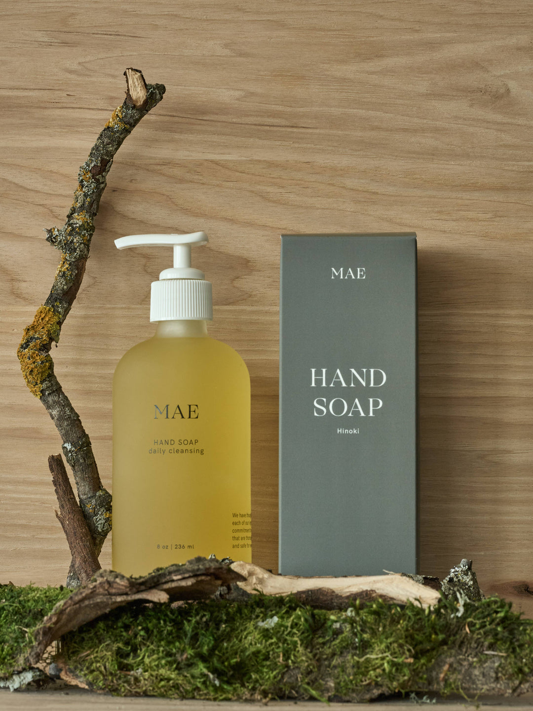 Hand soap bottle and packaging on a wooden surface with a branch and moss.