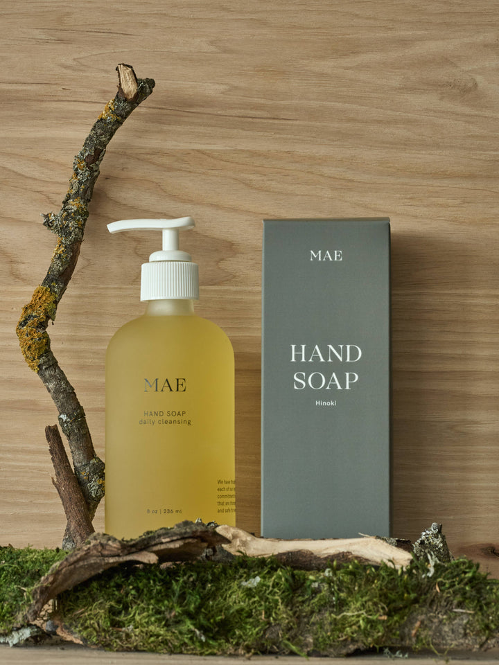Hand soap bottle and packaging on a wooden surface with a branch and moss.