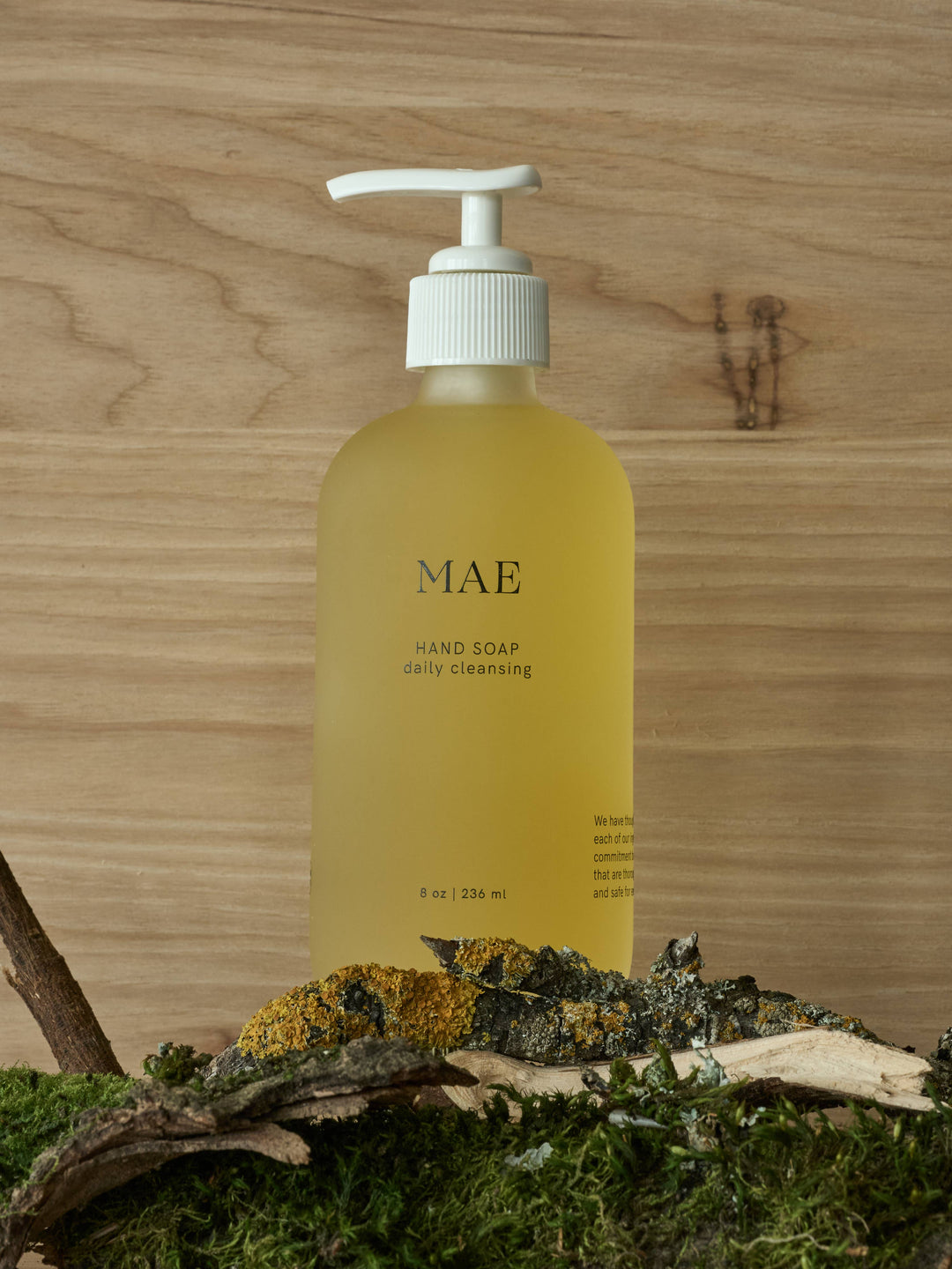Yellow bottle of MAE hand soap on a wooden surface with moss