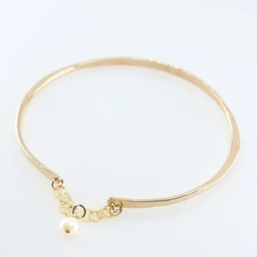 Gold bangle bracelet with safety chain and pearl accent on a white background