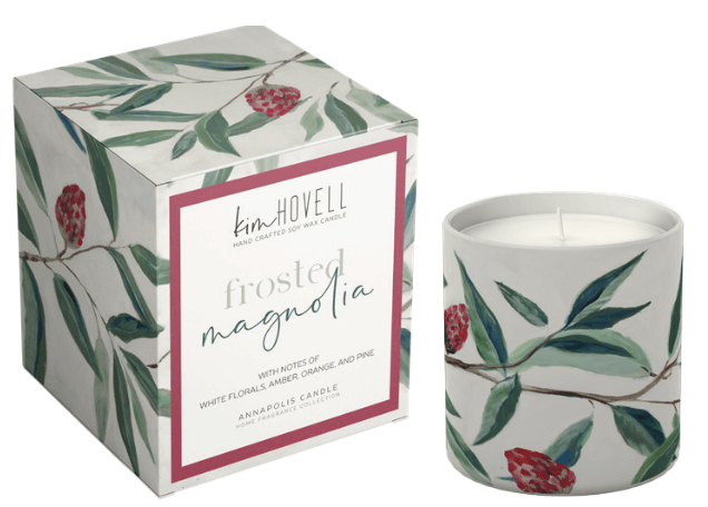 A frosted white candle in a matching cylindrical jar with a watercolor-style botanical print of green leaves and red berries, shown next to its square illustrated box. The box features a white front label with a pink border and the brand name 'kim HOVELL'.