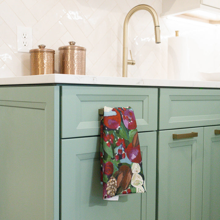 Kitchen with green cabinets, a colorful towel, and brass fixtures.