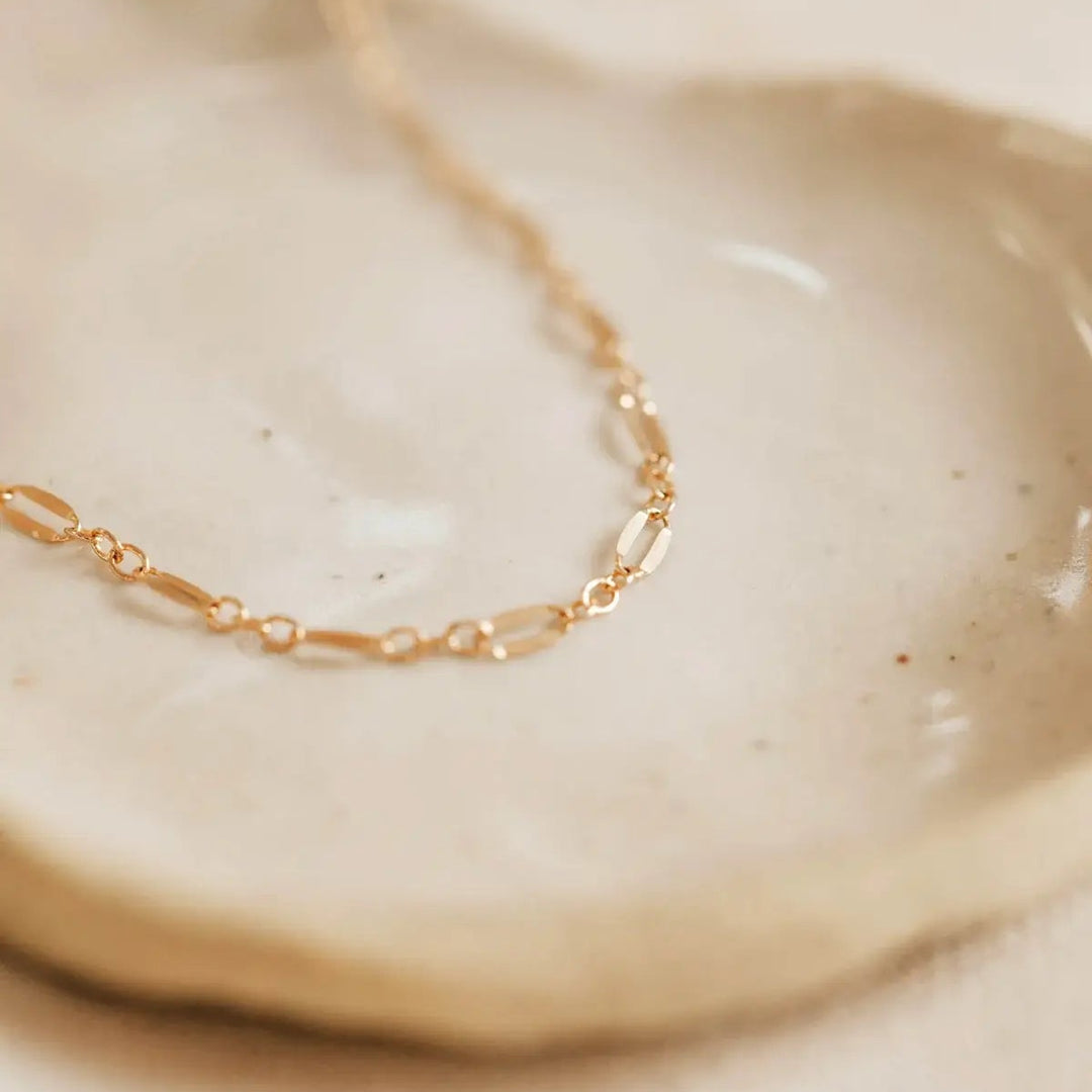 Gold chain bracelet on a beige ceramic dish