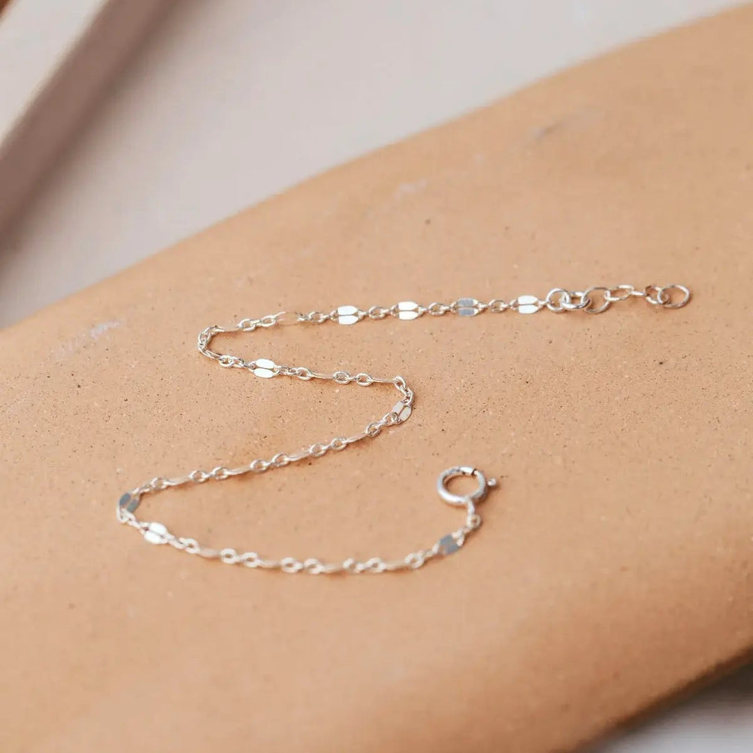 Silver chain necklace on a person's wrist against a neutral background