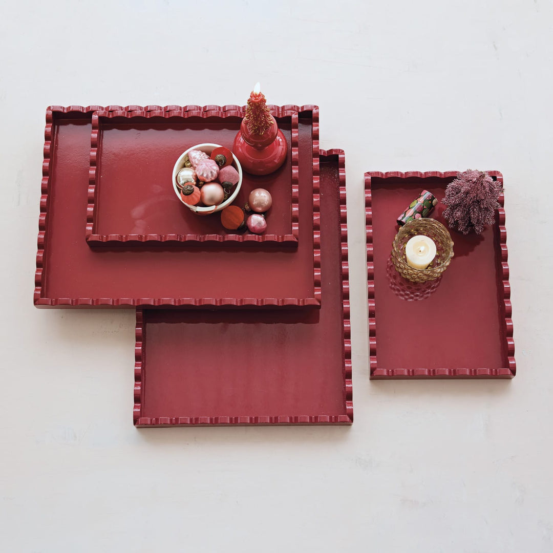 4 nested rectangular serving trays in a deep red color with a textured beaded border, styled with decorative objects on a light off-white background.