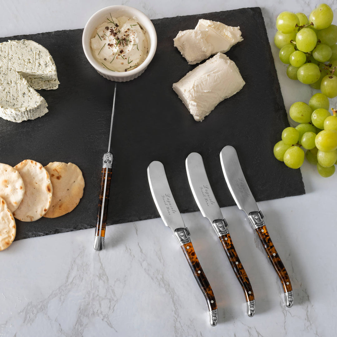 Cheese platter with cheeses, grapes, and tortoise shell handle cheese knives on a marble surface.