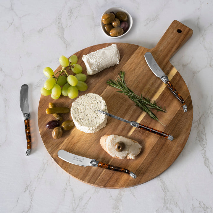 Wooden cutting board with cheese, grapes, olives, and tortoise shell handle knives on a marble surface