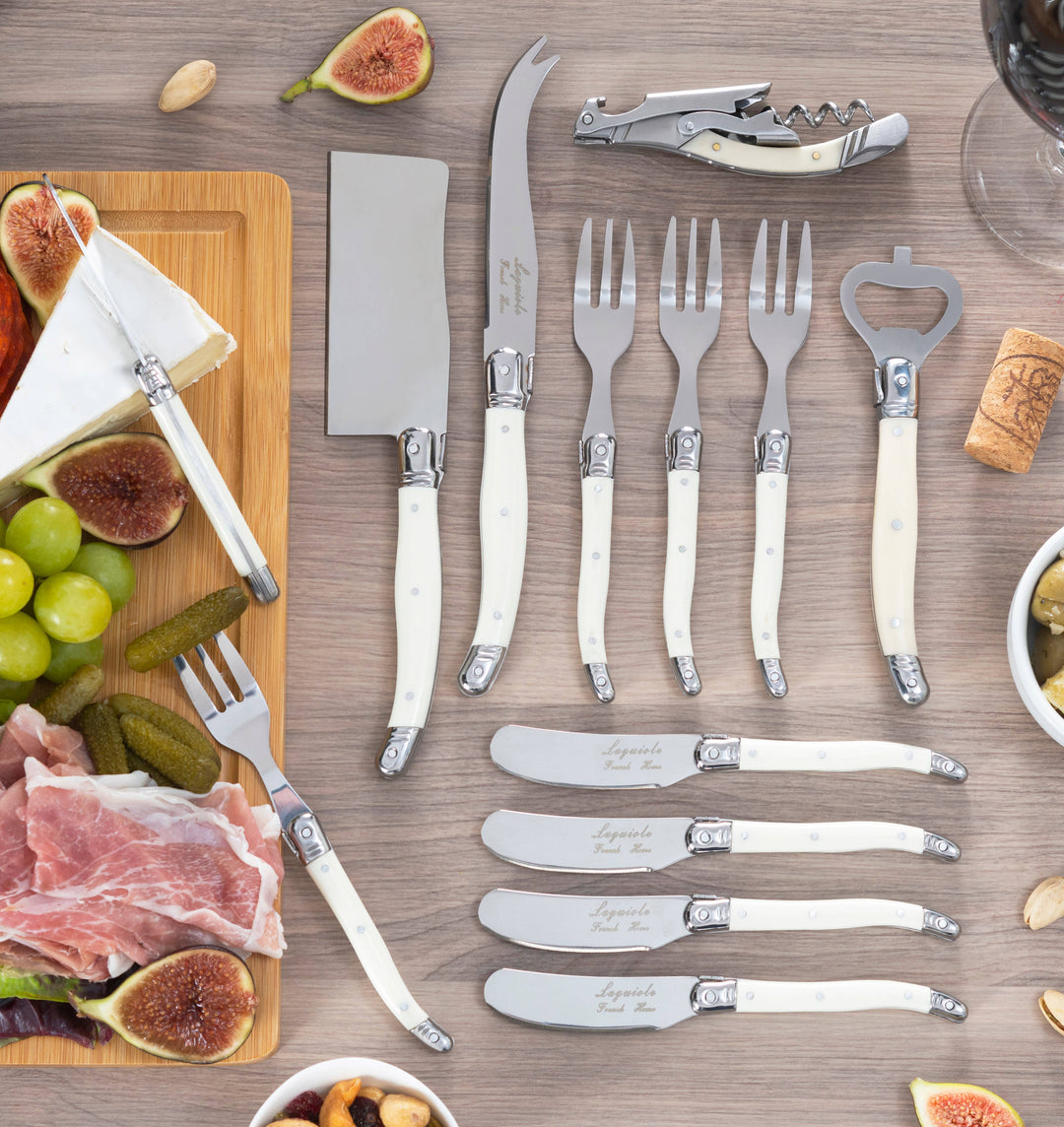 Set of knives, forks, and cheese knives with faux ivory handles on a wooden surface with food items.