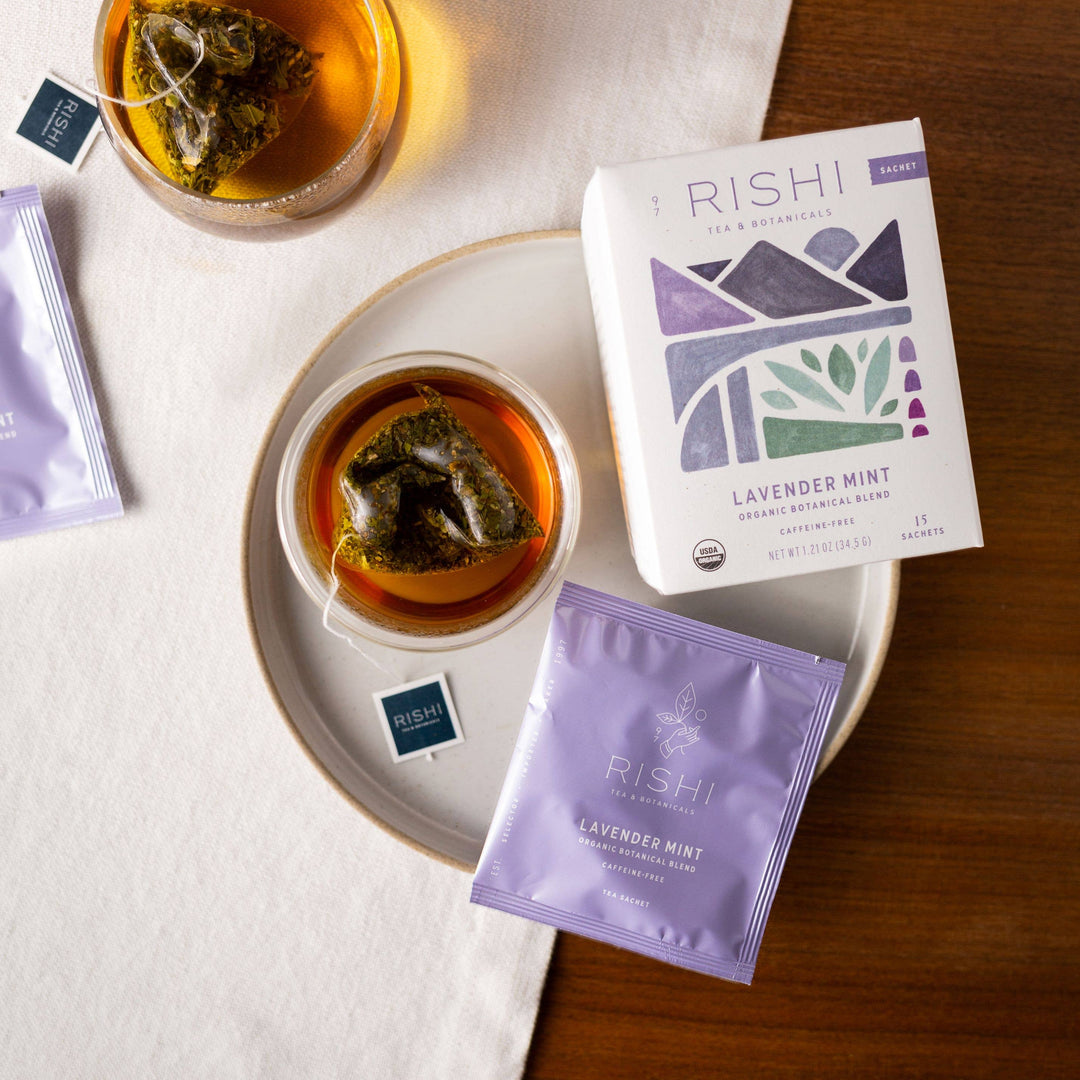 Rishi Lavender Mint tea packaging with two cups of tea and loose tea leaves on a wooden surface.