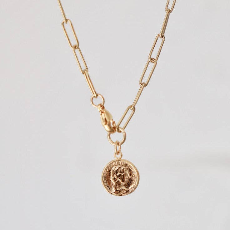Gold necklace with a coin pendant on a light gray background