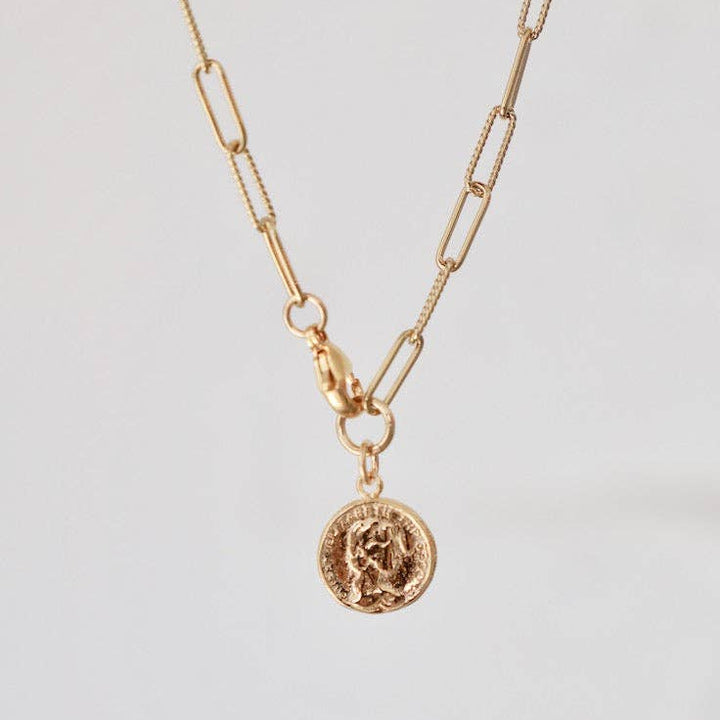 Gold necklace with a coin pendant on a light gray background