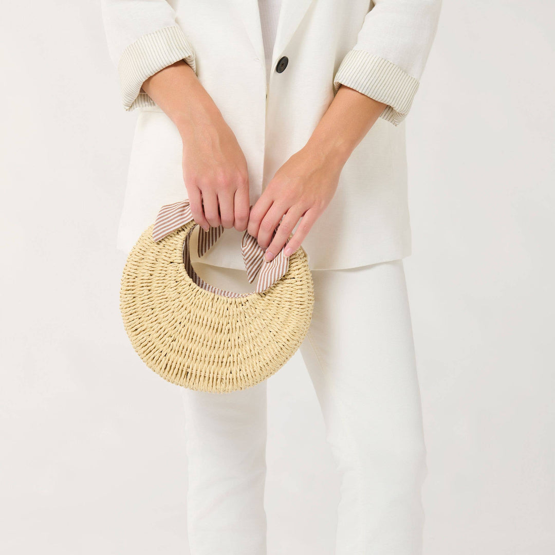 Person holding a woven handbag wearing a white outfit on a plain background