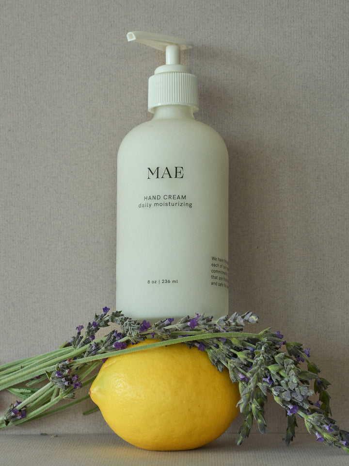 Hand cream bottle labeled 'MAE' with a lemon and lavender on a neutral background