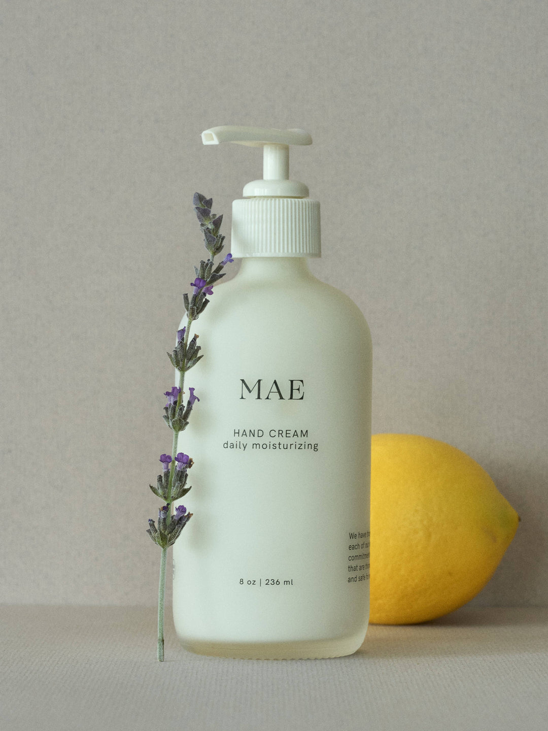 Hand cream bottle labeled 'MAE' with a lemon and lavender sprig on a neutral background