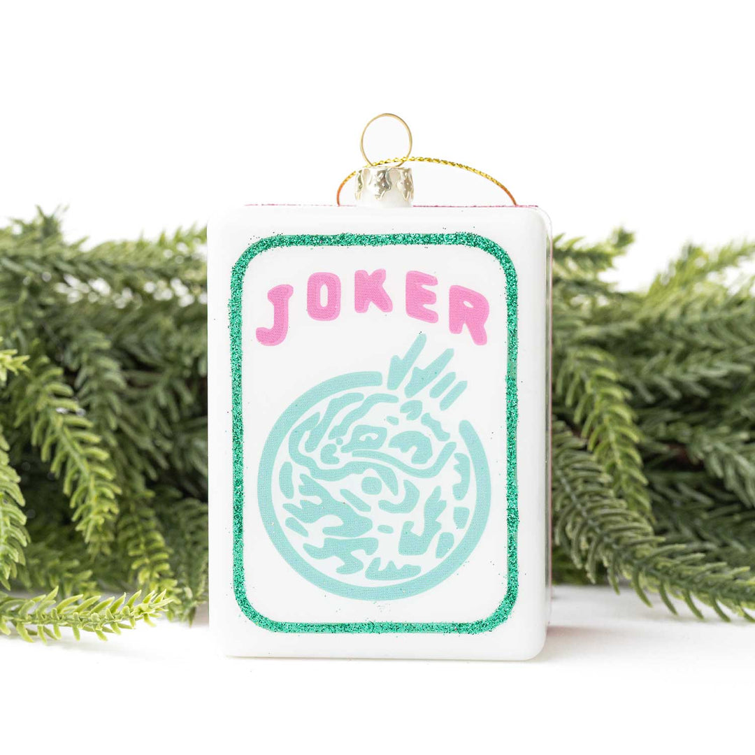 Decorative card with 'Joker' text and design, hanging against a white background with greenery.