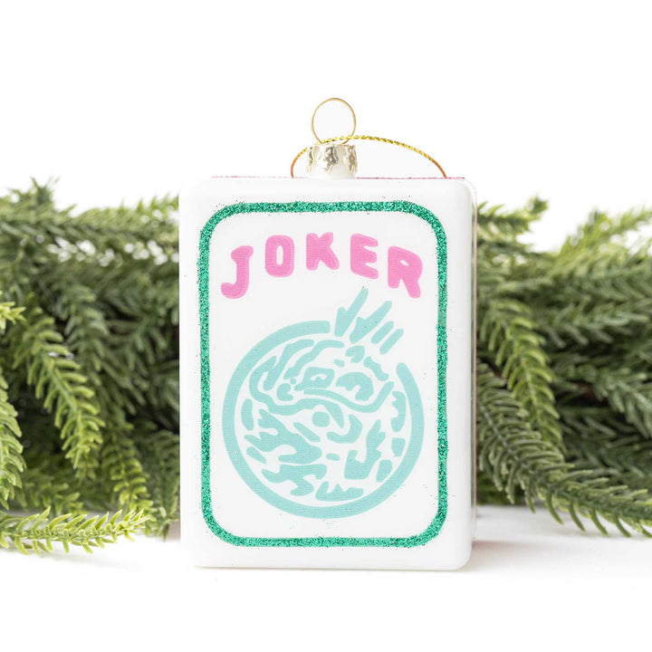 Decorative card with 'Joker' text and design, hanging against a white background with greenery.