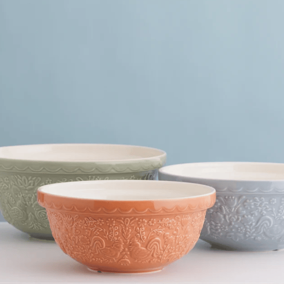 Three embossed ceramic bowls in sage green, terracotta orange, and light blue, arranged on a white surface against a soft light blue background.