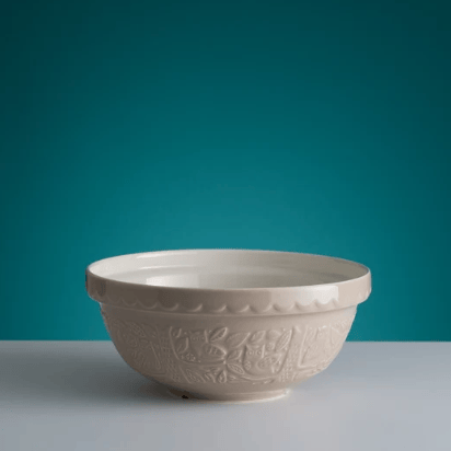 An off-white ceramic bowl with embossed floral patterns and a scalloped rim, set against a teal background and a light gray surface.