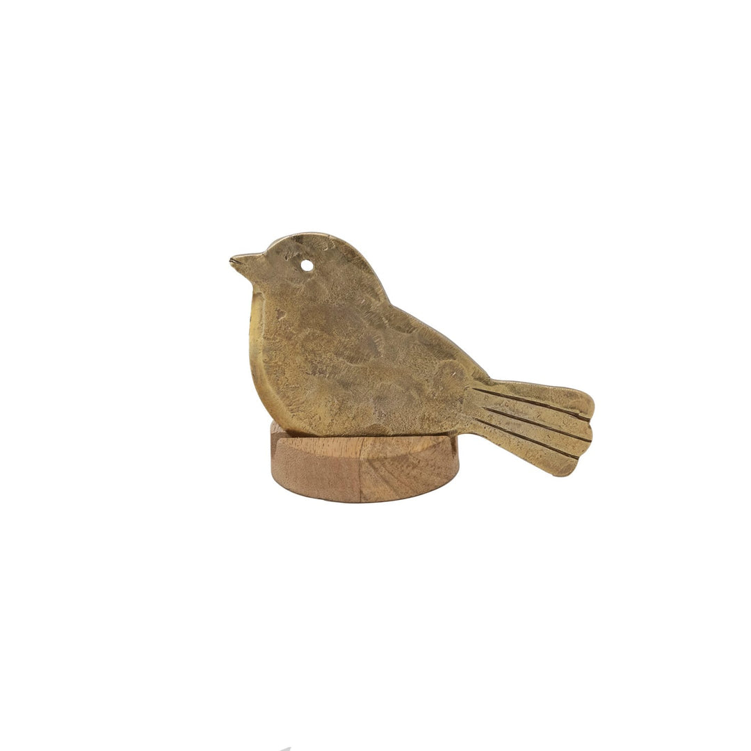 A small bird-shaped decorative object in a weathered gold or bronze finish, perched on a round wooden base against a plain white background.
