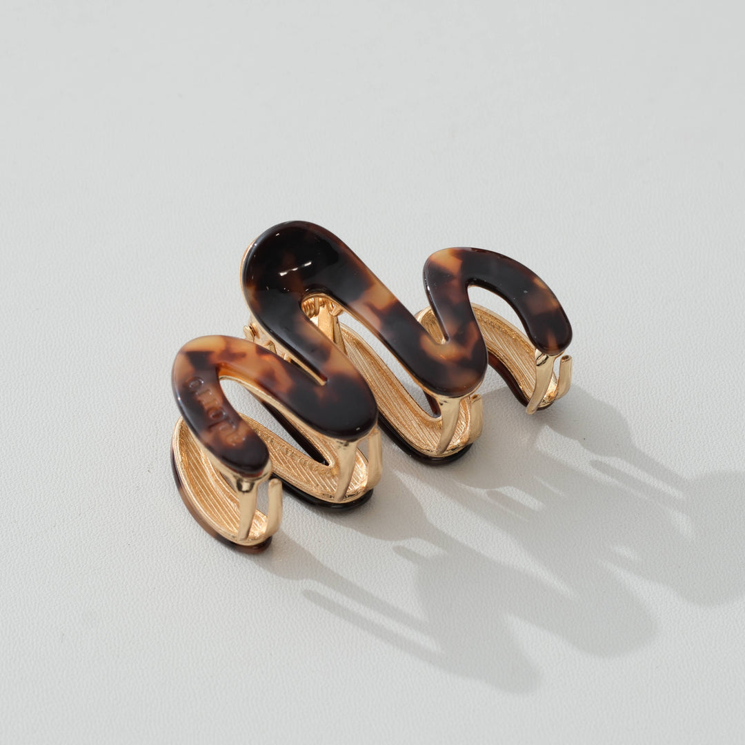Pair of tortoiseshell and gold claw hair clip on a light gray background