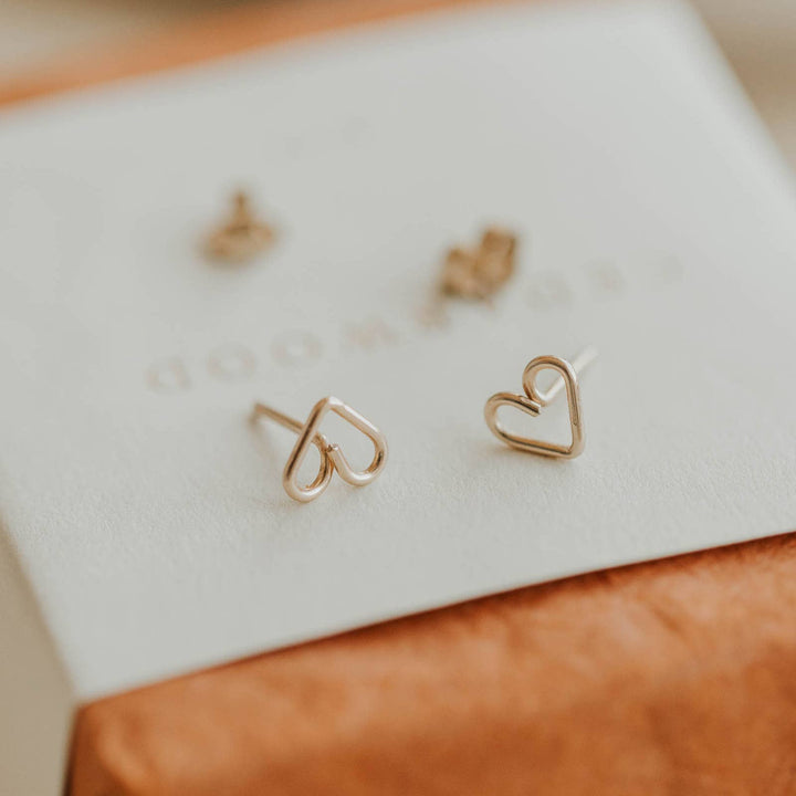Heart-shaped gold earrings on a white cloth with a brown surface underneath