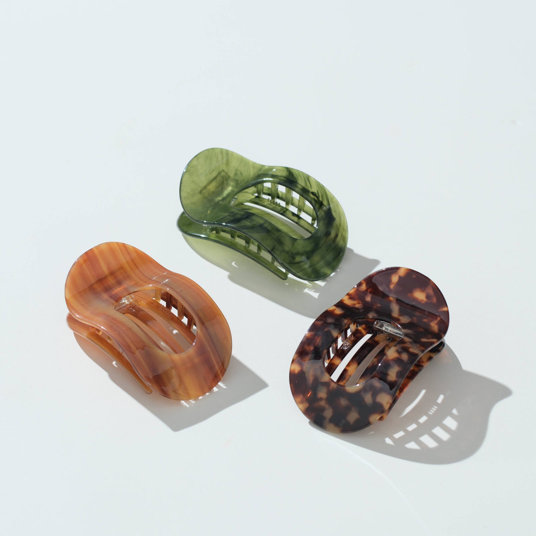 Three translucent hair claw clips in amber-brown, olive green, and tortoiseshell patterns, arranged on a clean white background with soft shadows.