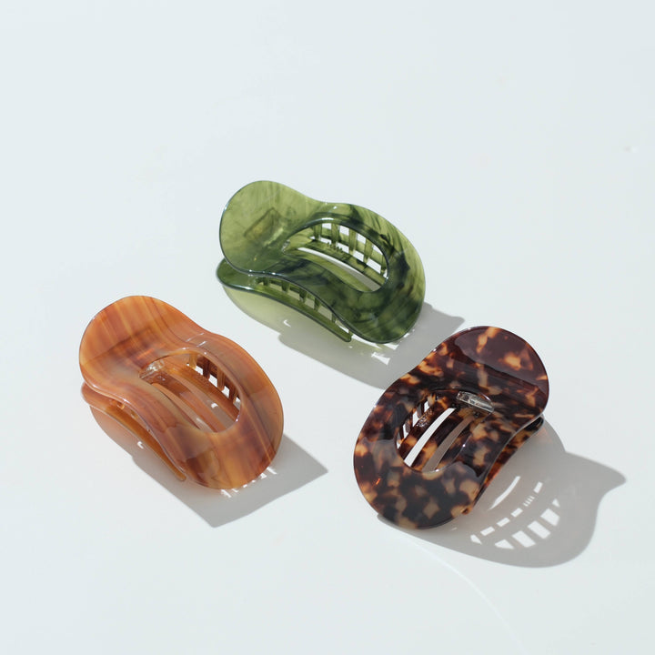 Three translucent hair claw clips in amber-brown, olive green, and tortoiseshell patterns, arranged on a clean white background with soft shadows.