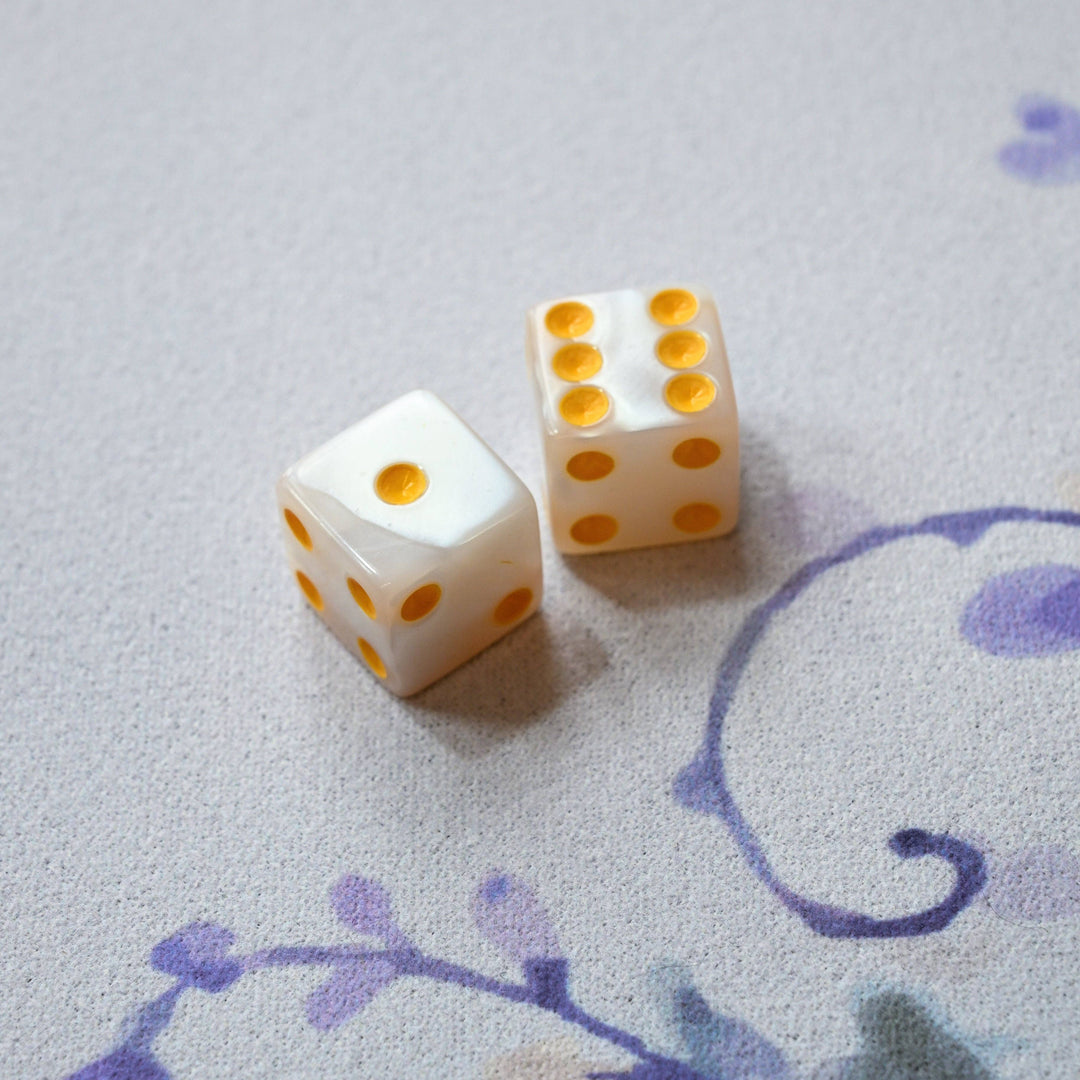 Two white dice with yellow dots on a textured surface with floral patterns