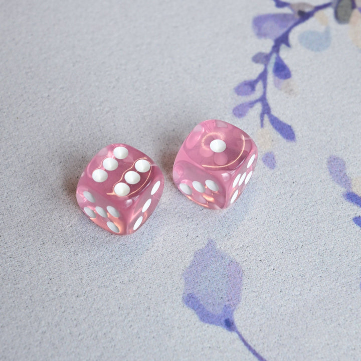 Two pink dice with white pips on a light gray surface with floral designs.