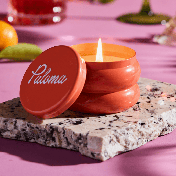 Orange candle with 'Paloma' lid on a pink surface