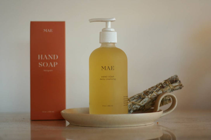 Yellow bottle of hand soap with pump and 'MAE' branding on a beige surface.