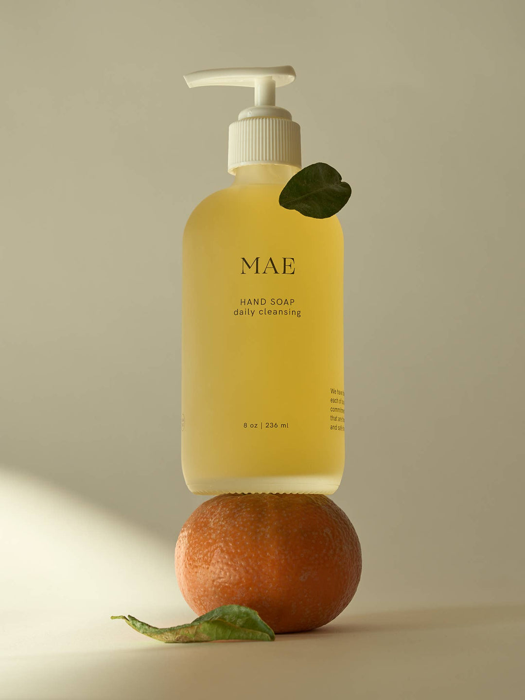 Yellow hand soap bottle labeled 'MAE' on a beige background with an orange and leaf.