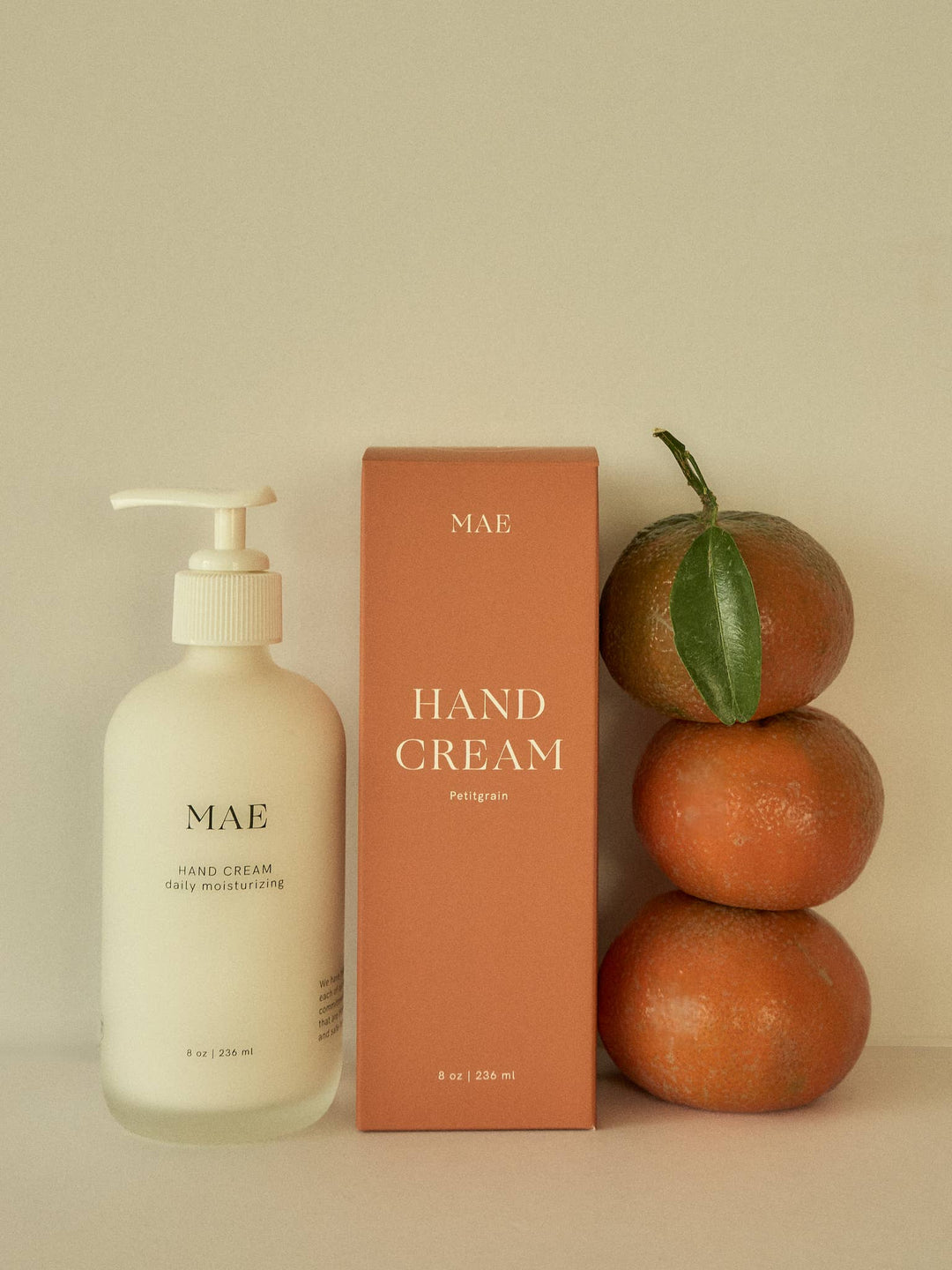 Mae hand cream bottle and packaging with oranges on a beige background