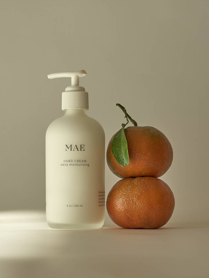 MAE hand cream bottle with two oranges on a beige background