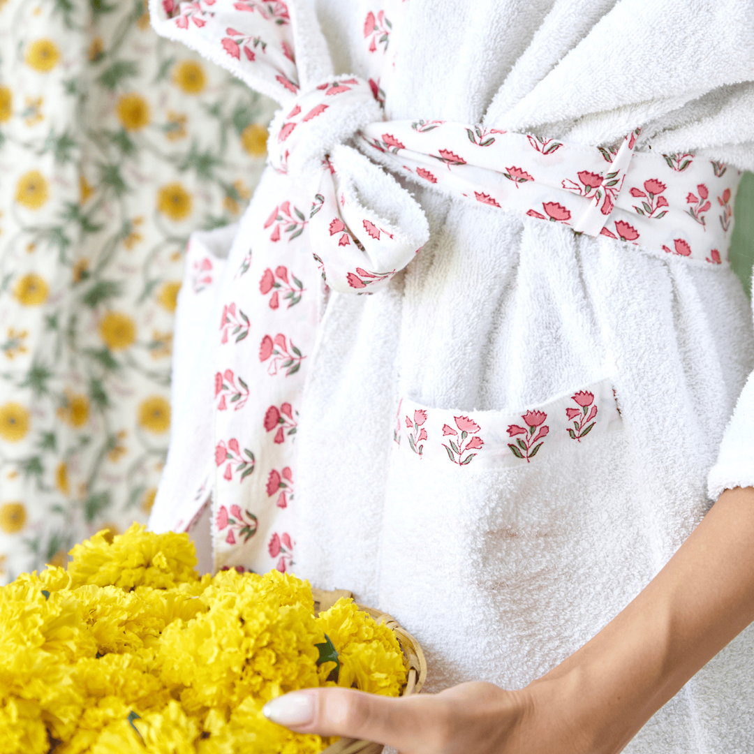 Person holding a basket of yellow flowers wearing a white robe with floral patterns.