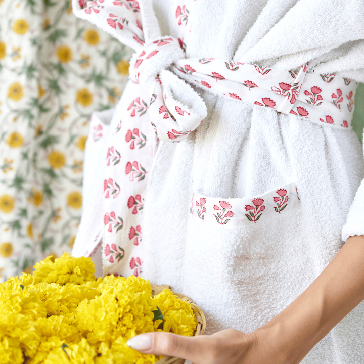 Person holding a basket of yellow flowers wearing a white robe with floral patterns.