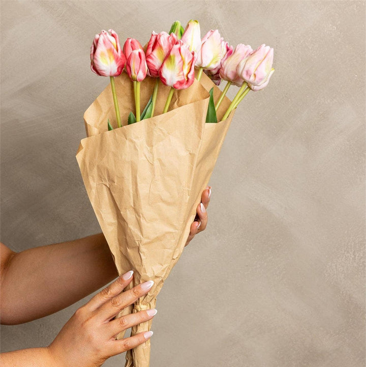 Bouquet of pink tulips wrapped in brown paper held by a person against a beige background
