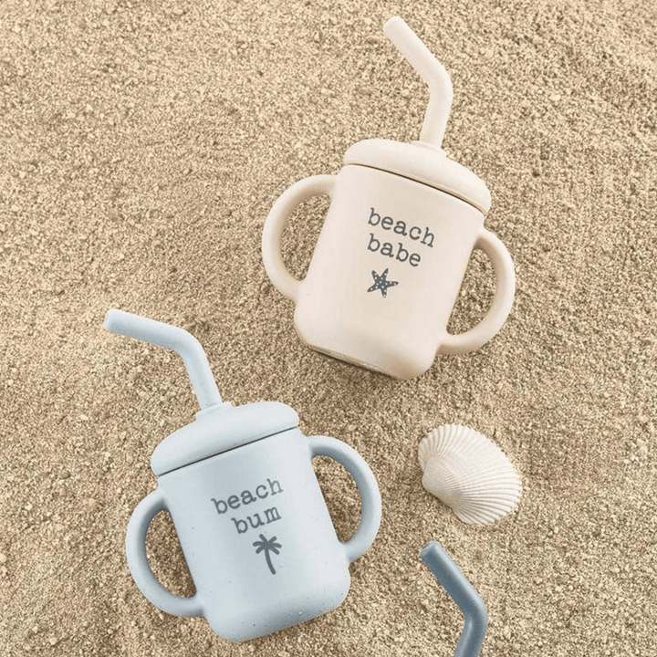 Pink and Blue Sippy Cups on sand with a seashell