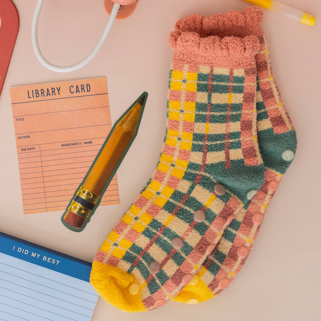 Plaid socks with a pen, library card, and notepad on a pink background