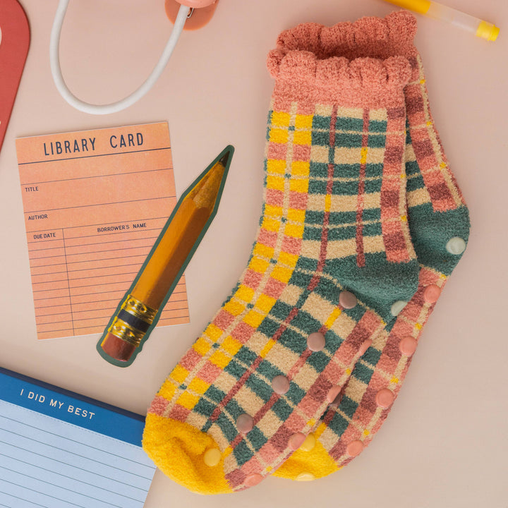 Plaid socks with a pen, library card, and notepad on a pink background