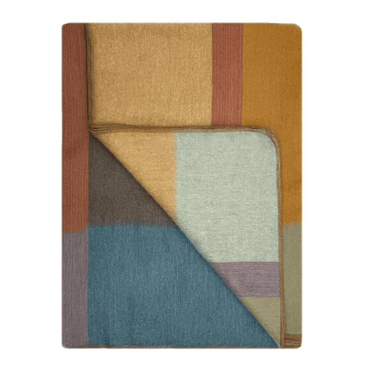 A folded woven throw blanket with a multicolor geometric block pattern, featuring shades of mustard yellow, dusty blue, brown, and light gray on a white background.