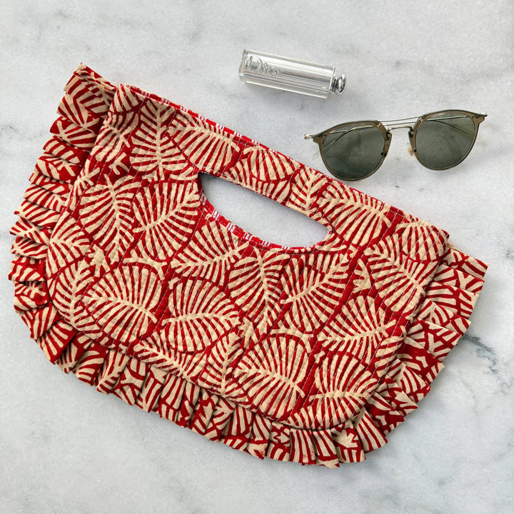 Red and white patterned bag with sunglasses and a bottle on a marble surface