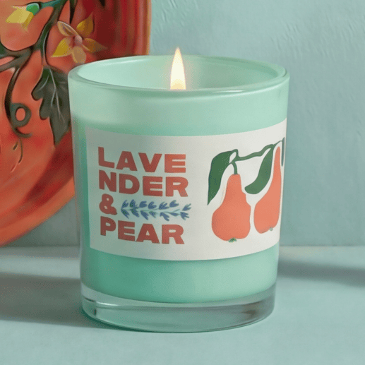 Candle in a green jar with a label reading 'Lavender & Pear' on a light blue background.