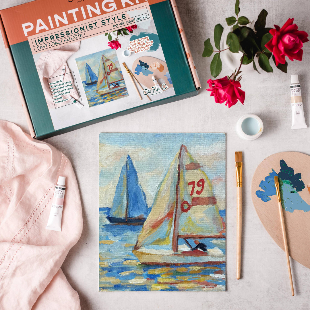 Painting kit with sailboat painting, brushes, and flowers on a table