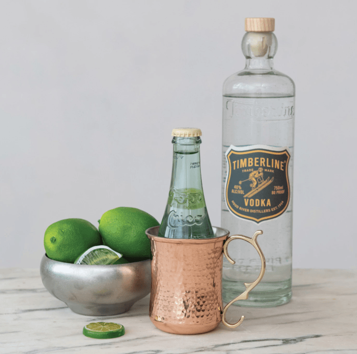 Bottle of Timberline Vodka, copper mug, and limes on a marble surface